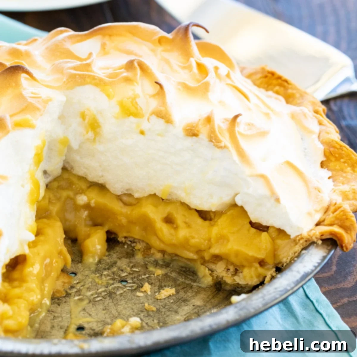 A delectable slice of Butterscotch Pudding Pie, showcasing its creamy filling and tall, golden meringue topping, with the rest of the pie in the background.
