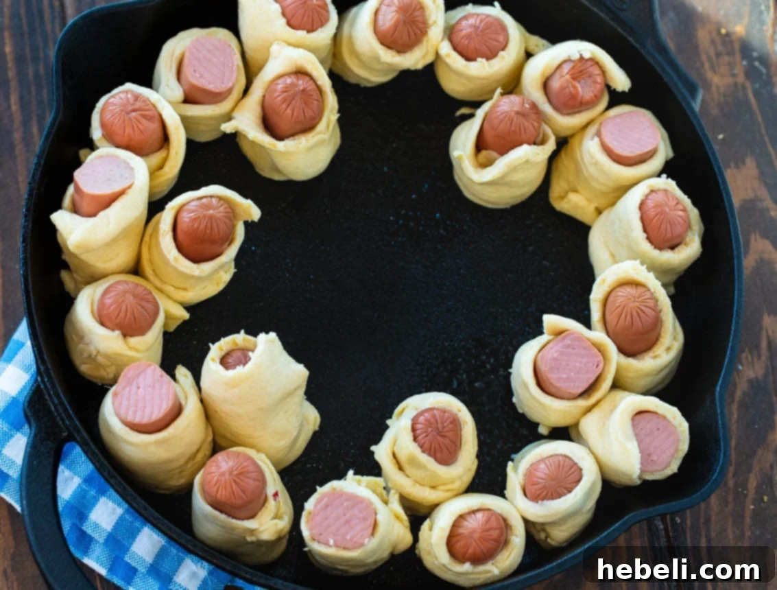 Hot dog pieces wrapped in dough arranged around the edge of a cast iron skillet before baking.