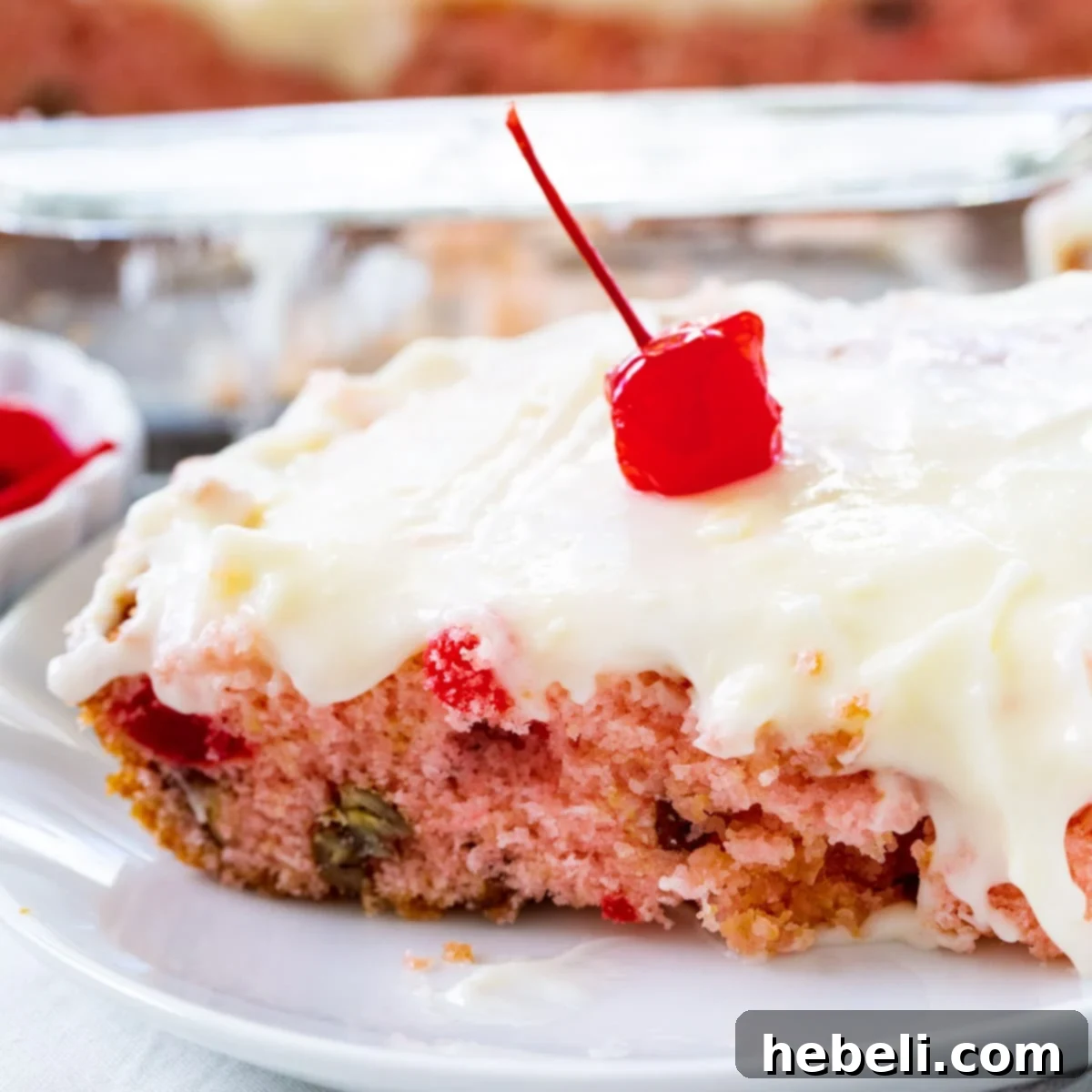A perfectly sliced piece of Cherry Sheet Cake, topped with a bright red maraschino cherry, served elegantly on a white plate, showcasing its fluffy texture and rich icing.