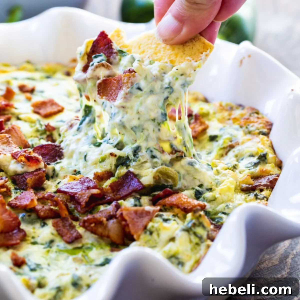 Fiery Jalapeno Bacon Spinach Dip 2 Chip scooping up a generous amount of hot jalapeño bacon spinach dip, showing its creamy texture and bits of bacon and spinach.