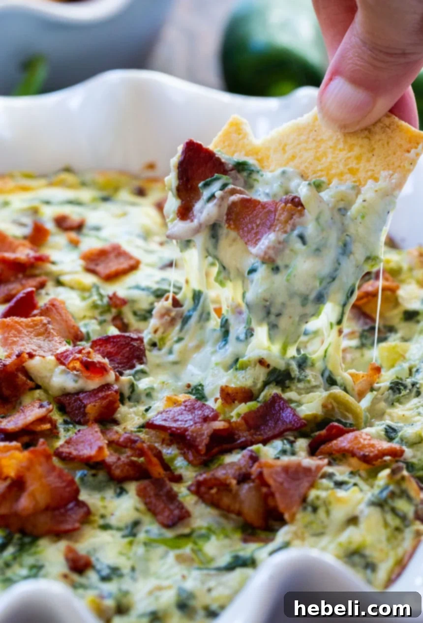 Fiery Jalapeno Bacon Spinach Dip 4 A bowl of hot jalapeño bacon spinach dip with pita chips and fresh vegetables on the side, ready to be served.