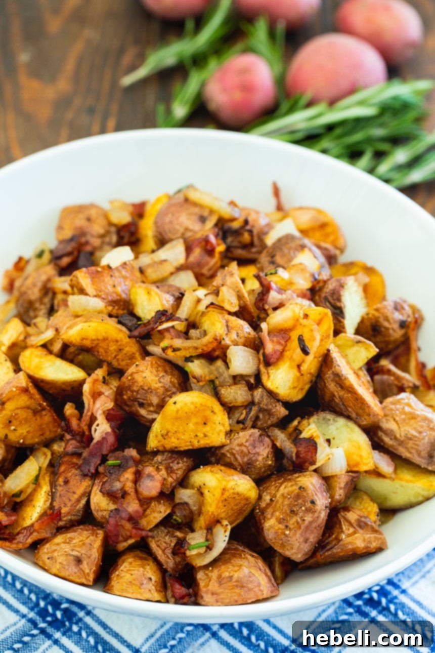 Italian Roasted Potatoes in a white bowl with fresh red potatoes and rosemary sprigs in the background.