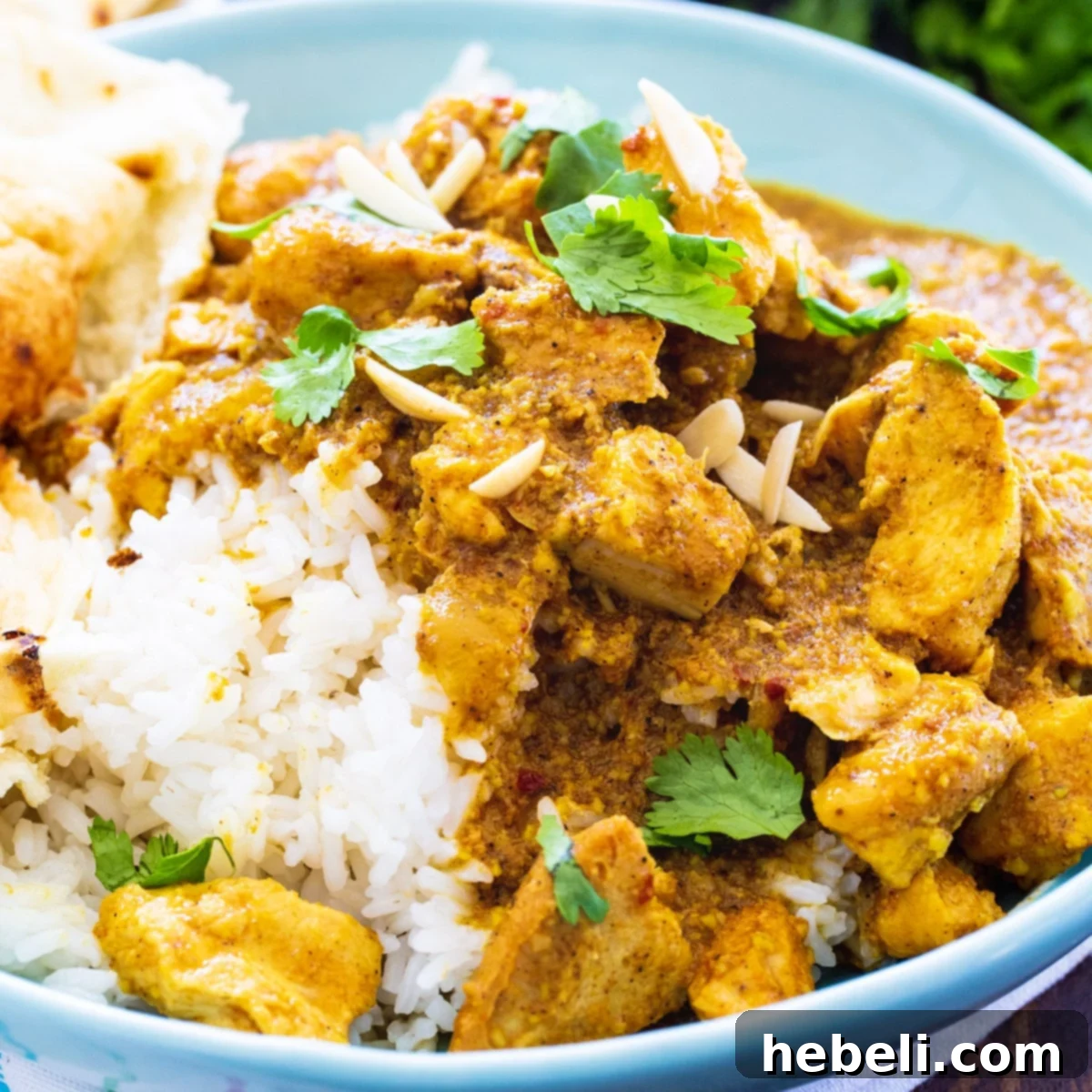 Creamy Slow Cooker Chicken Korma served over white rice in a blue bowl, garnished with fresh cilantro.