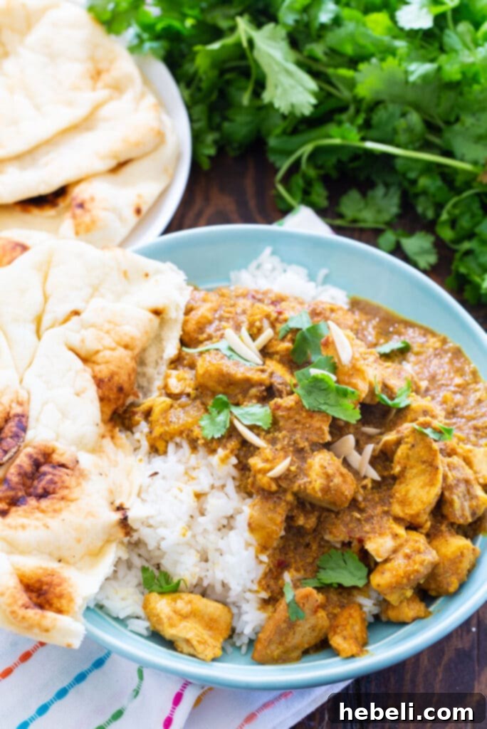 A bowl of Slow Cooker Chicken Korma over rice, accompanied by a piece of naan bread and fresh cilantro garnish.