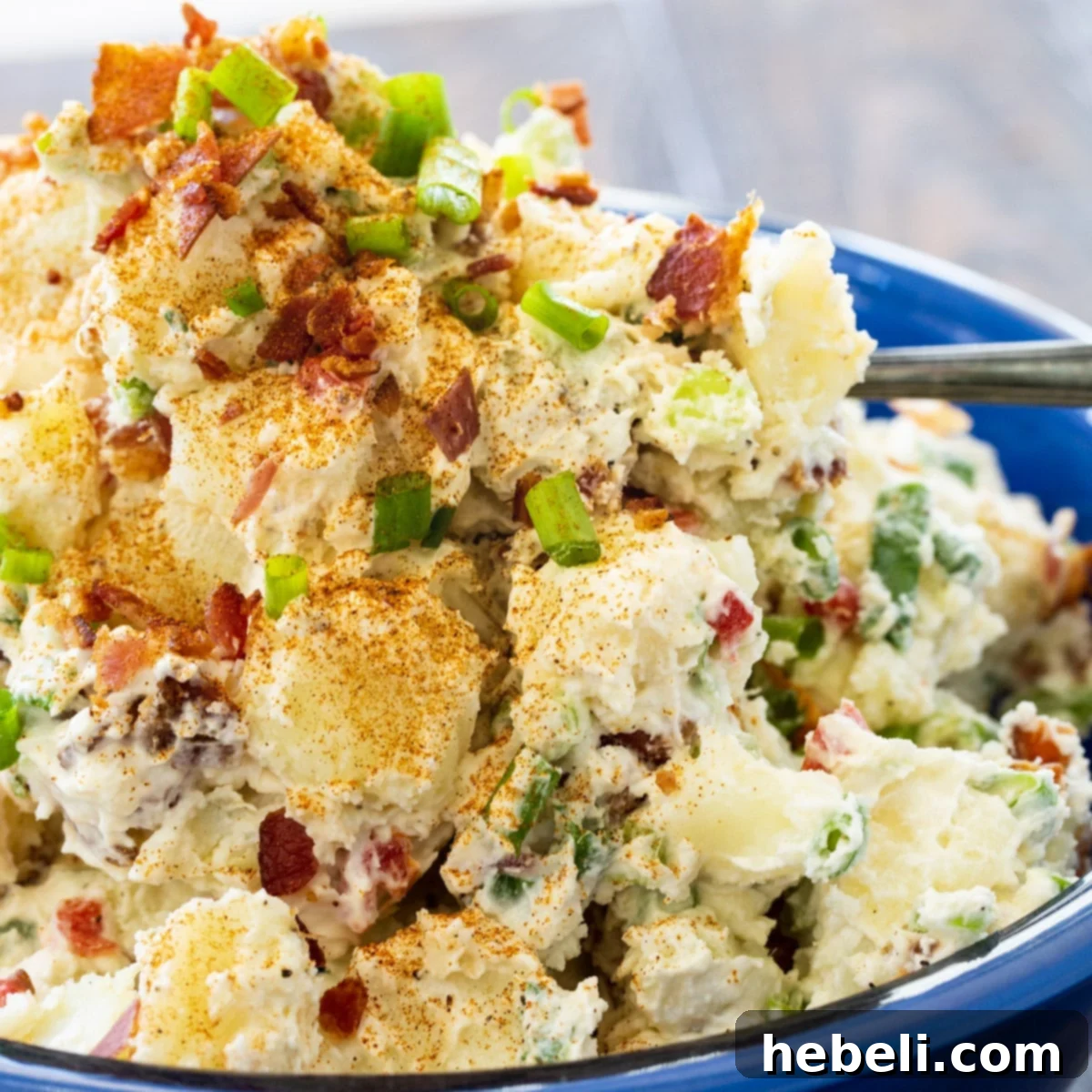 Loaded Bacon Potato Salad 2 Large blue bowl filled with creamy bacon potato salad, garnished with green onions and paprika, ready for serving at a cookout.