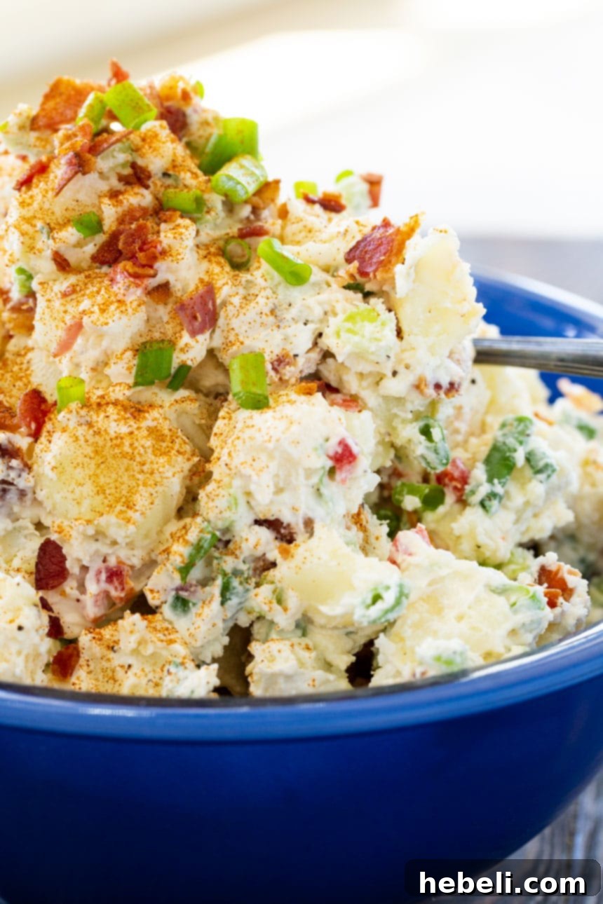 Loaded Bacon Potato Salad 4 Close-up of a serving of creamy bacon potato salad, garnished with green onions and paprika, showcasing the crispy bacon bits.