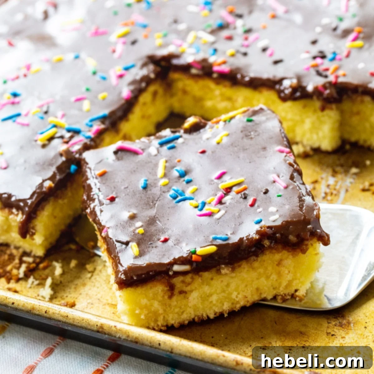 Spatula lifting a generous piece of Cream Cheese Sheet Cake from a baking pan