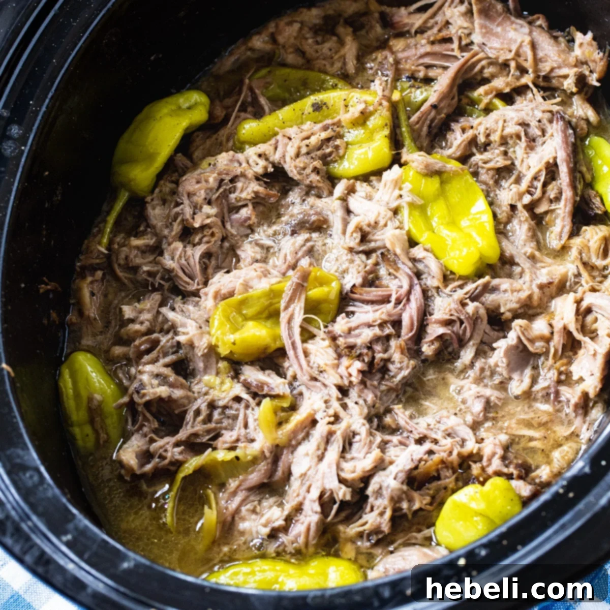 Close-up of Slow Cooker Mississippi Pulled Pork with vibrant pepperoncini peppers in a crock pot, ready to be shredded.