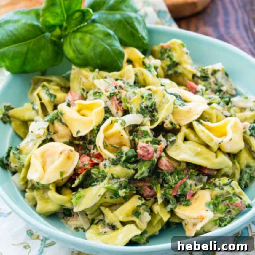 A vibrant blue bowl filled with Creamy Spinach Tortellini, garnished with fresh basil leaves, ready to be enjoyed.