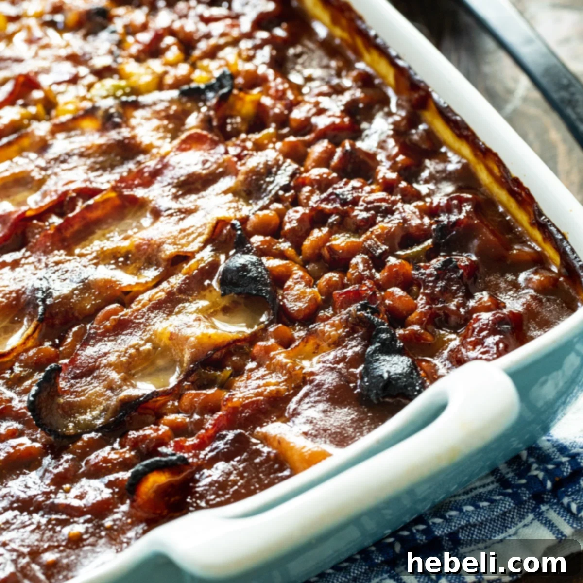 Molasses Baked Beans generously topped with crispy bacon in a rustic white baking dish, perfect for a cookout.