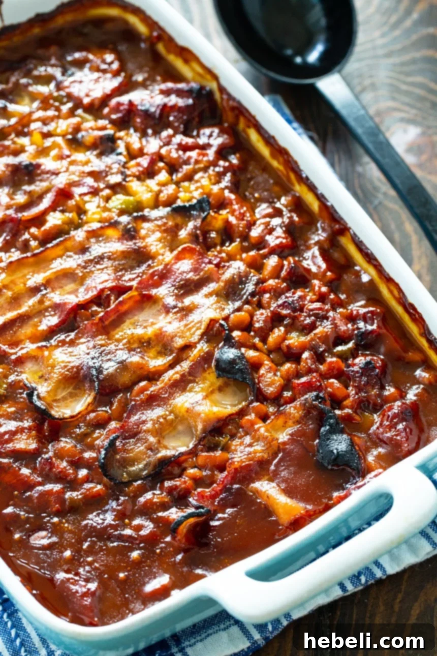 A close-up view of Molasses Baked Beans featuring a thick, rich sauce and strips of perfectly cooked bacon in a baking dish.