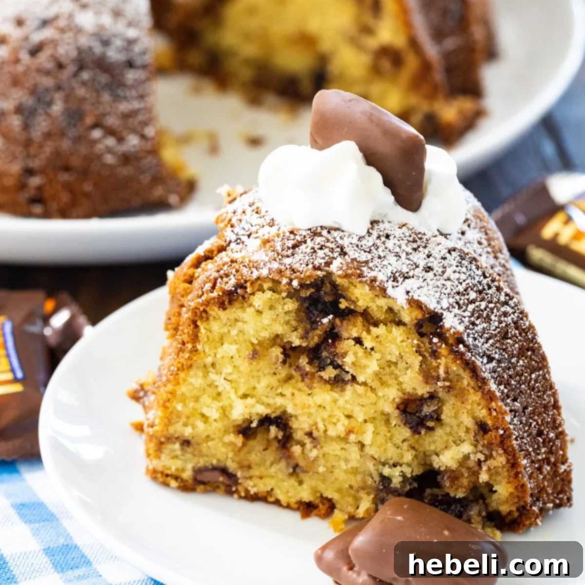A delectable slice of Toffee Bundt Cake on a pristine white plate, showcasing its moist interior and generous distribution of chocolate chips and toffee bits.