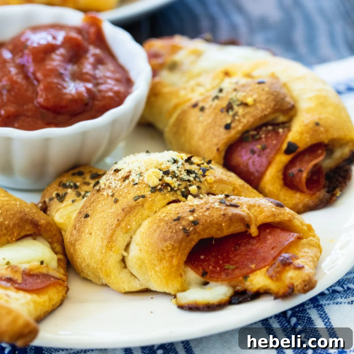 Golden brown Pepperoni Crescent Rolls artfully arranged on a white plate, with a small bowl of marinara sauce ready for dipping.