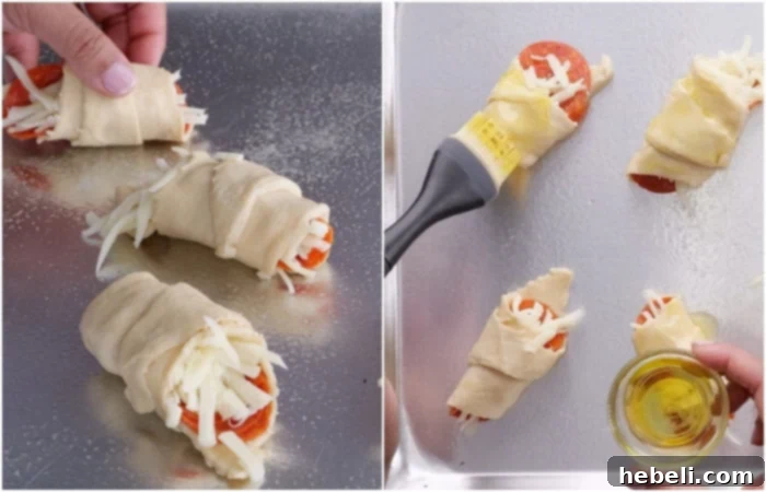 Rolled crescent rolls, filled with pepperoni and cheese, arranged on a baking sheet and brushed with olive oil, ready for seasoning and baking.