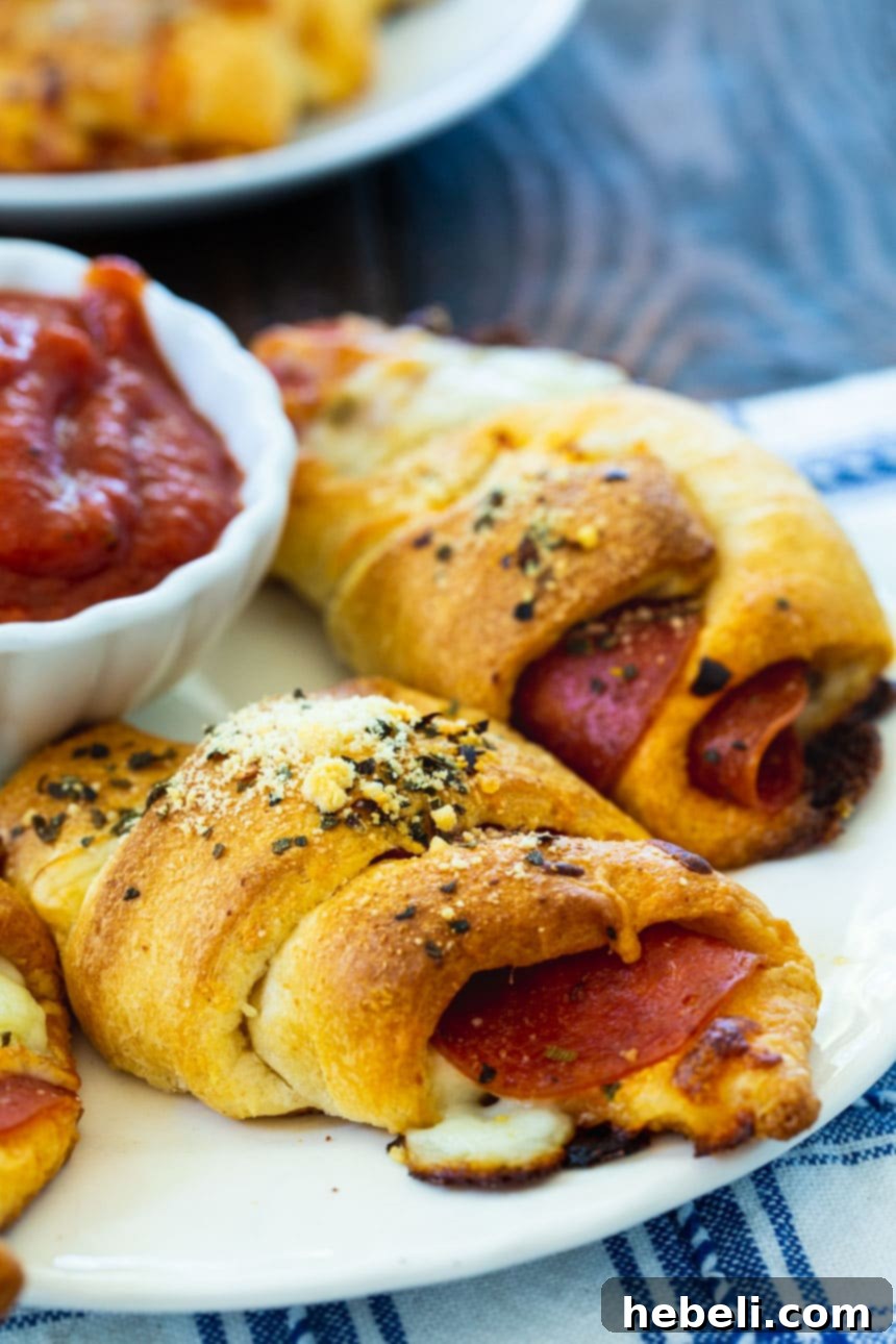A mouth-watering close-up of a Pepperoni Crescent Roll, revealing melted mozzarella and savory pepperoni peeking from its golden, flaky crust on a white plate.
