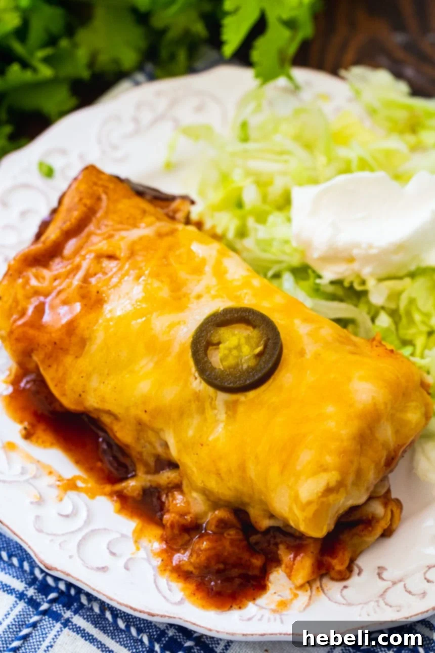 Slow Cooker Smothered Burrito on a plate with fresh shredded iceberg lettuce and a dollop of sour cream.