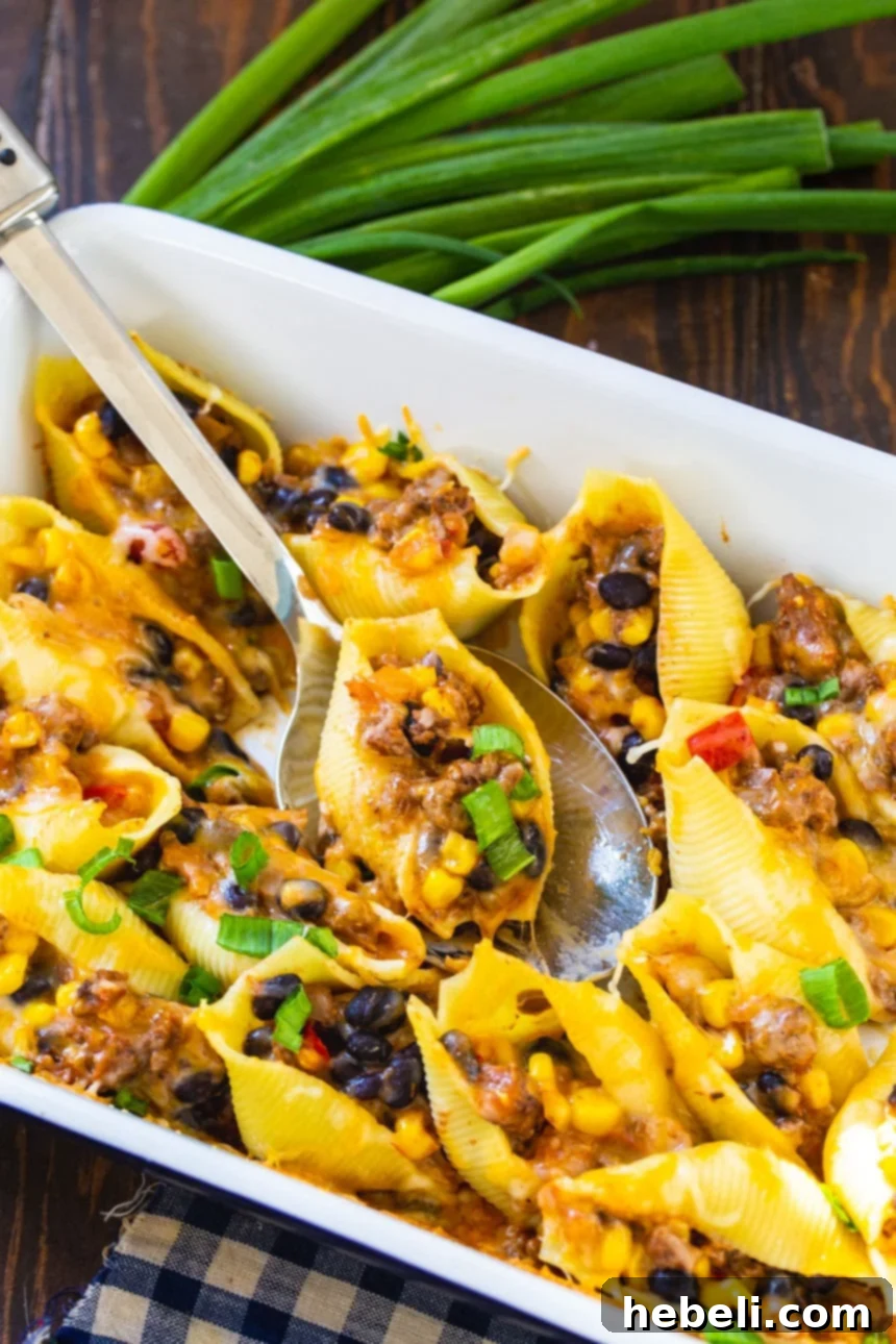 A serving spoon lifting a Taco Stuffed Shell from the baking dish, steam gently rising.
