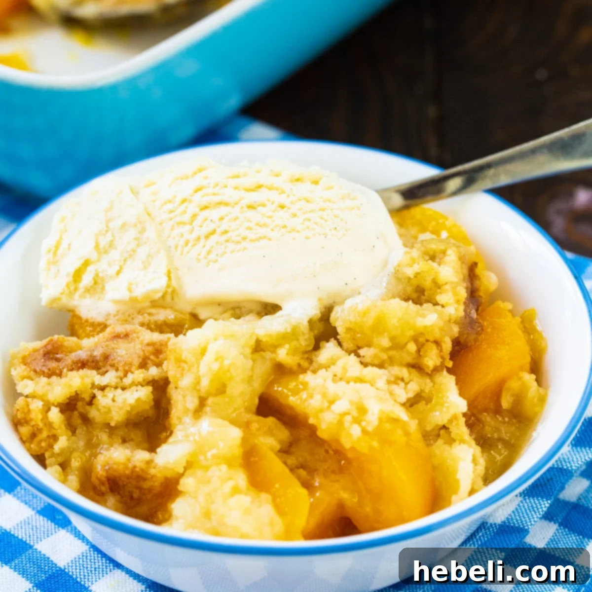 Year-Round Peach Cobbler Delight 2 Anytime Peach Cobbler in a bowl with vanilla ice cream, showcasing its golden crust and juicy peach filling.