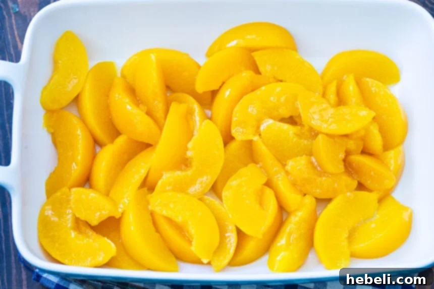 Year-Round Peach Cobbler Delight 4 Sliced canned peaches arranged neatly at the bottom of a baking dish, forming the base of the cobbler.