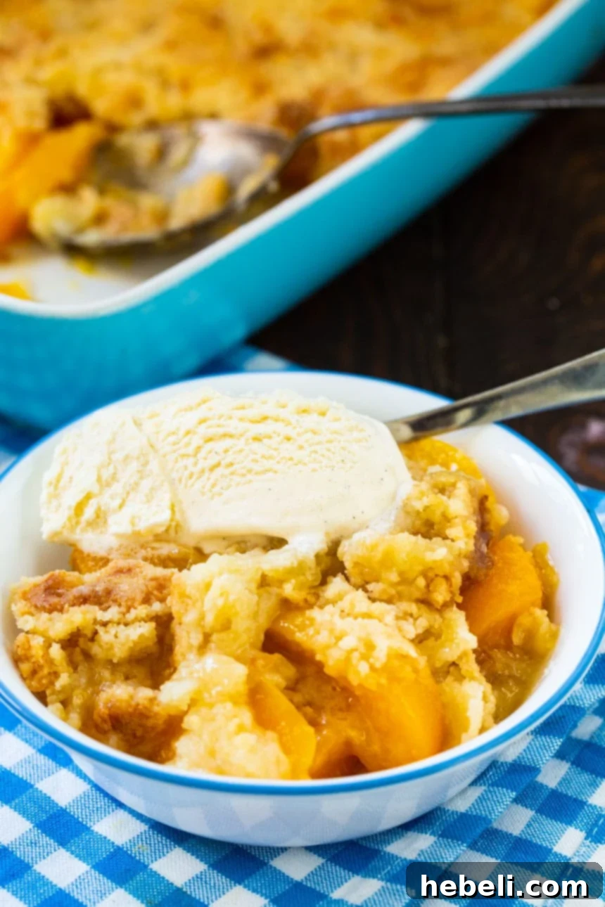 Year-Round Peach Cobbler Delight 5 A serving of warm Anytime Peach Cobbler in a bowl, with a scoop of melting vanilla ice cream and a spoon ready for enjoyment.
