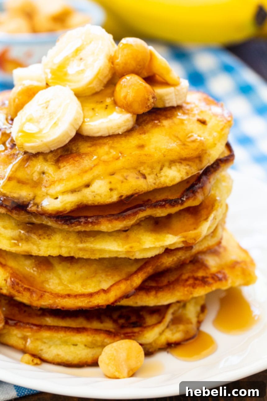 Close-up of a stack of golden Banana Macadamia Pancakes on a white plate, showcasing the texture and nuts within.