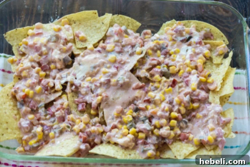 Ultimate Bacon and Egg Chilaquiles 3 Adding the creamy salsa and corn mixture to a layer of tortilla chips in a baking dish.