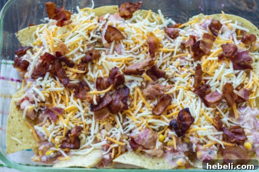 Ultimate Bacon and Egg Chilaquiles 4 Layering shredded cheese and crumbled bacon over the salsa and chips in a baking dish for chilaquiles.