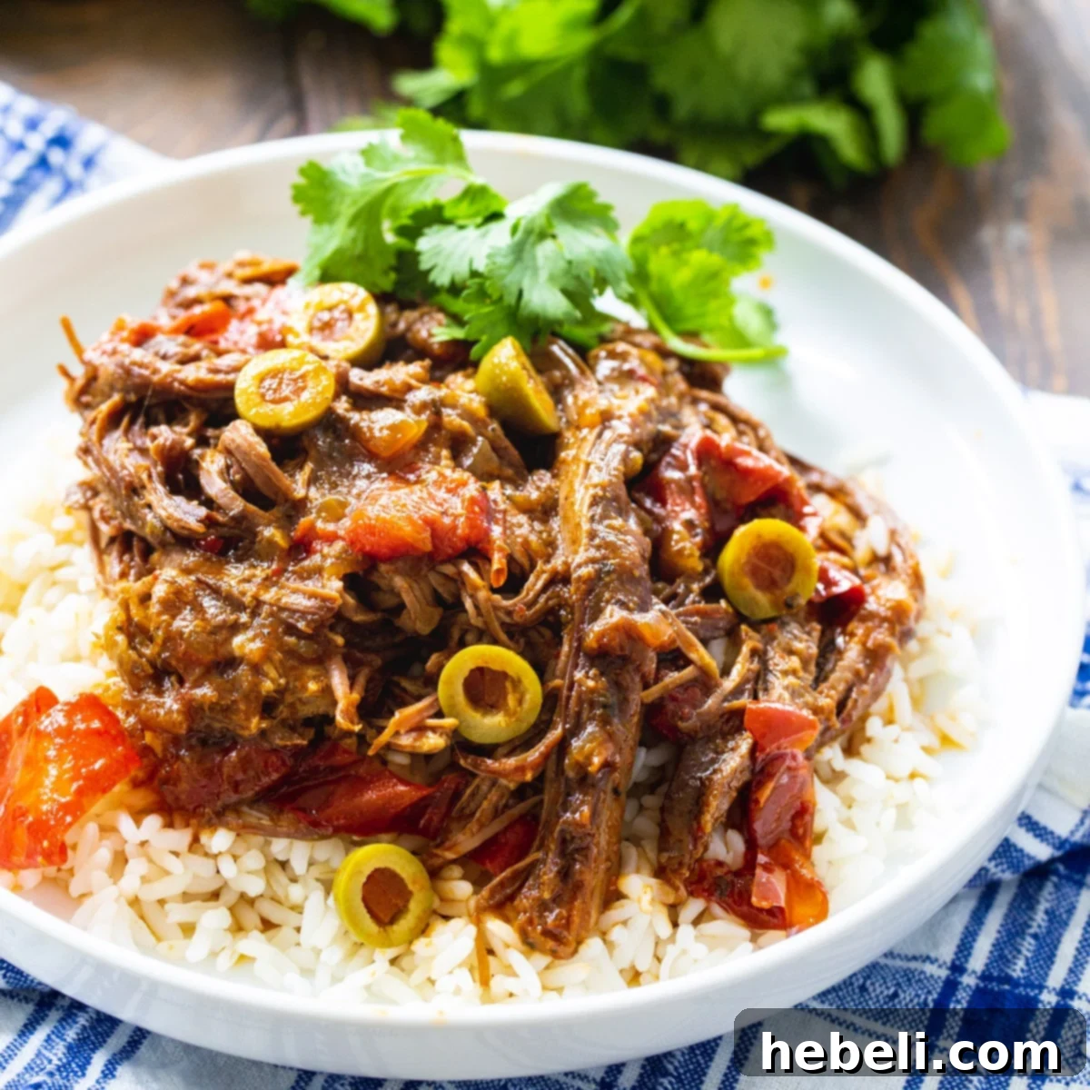 Slow Cooker Ropa Vieja served over rice on a plate, garnished with fresh cilantro.