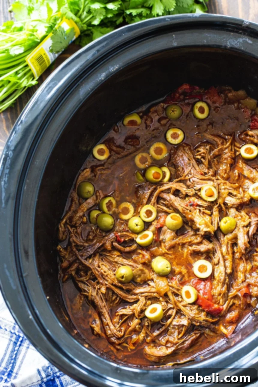 Ropa Vieja simmering in a black crock pot, ready to be shredded.
