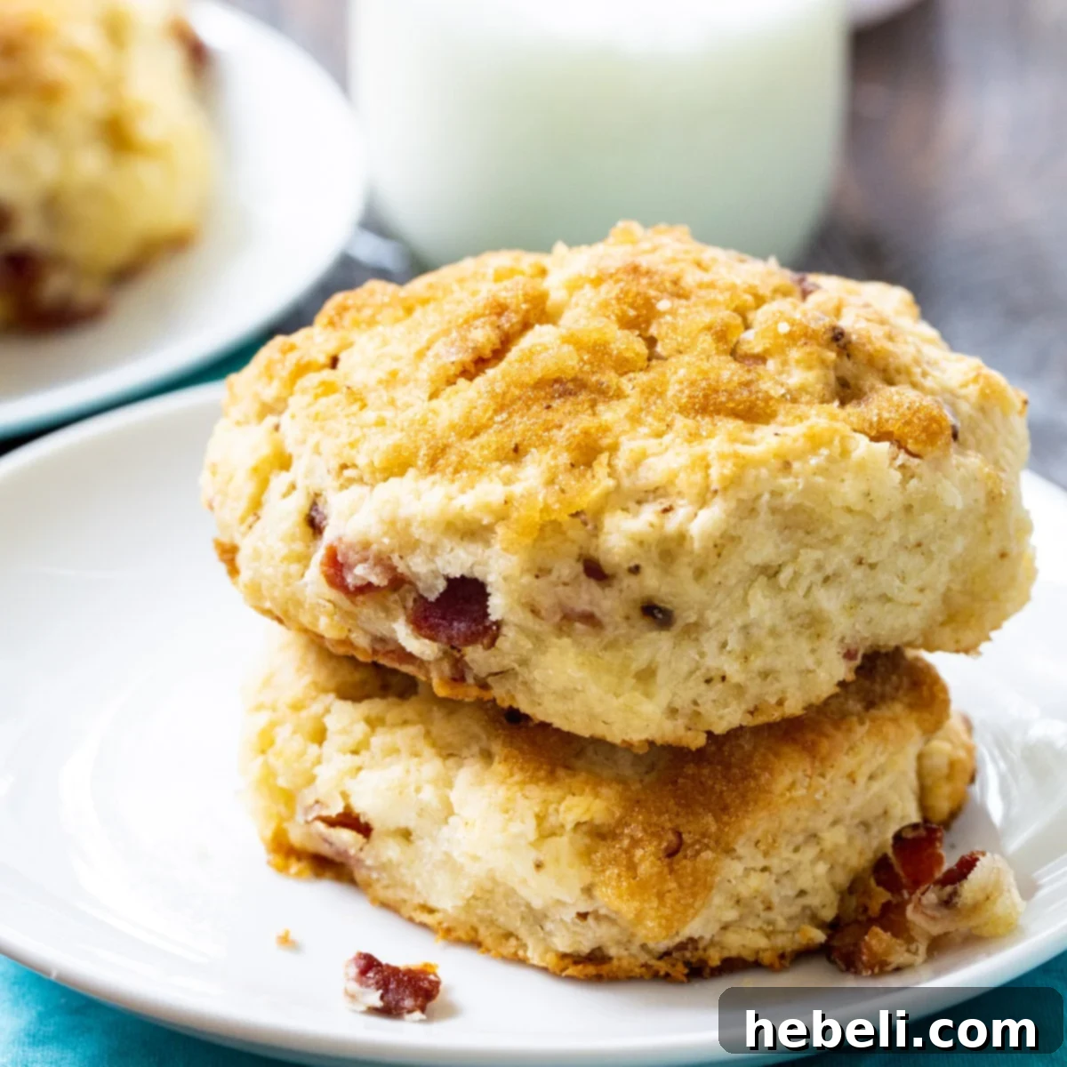 Two golden-brown Brown Sugar and Bacon Biscuits resting on a white plate, showcasing their fluffy texture and delicious bacon bits.