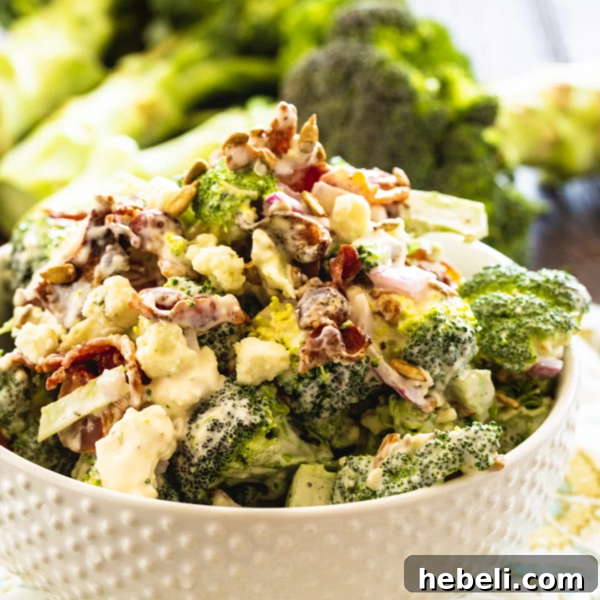 A vibrant bowl of Bacon Blue Cheese Broccoli Salad, featuring green broccoli, red onion, white blue cheese, and golden bacon bits, all coated in a creamy dressing.