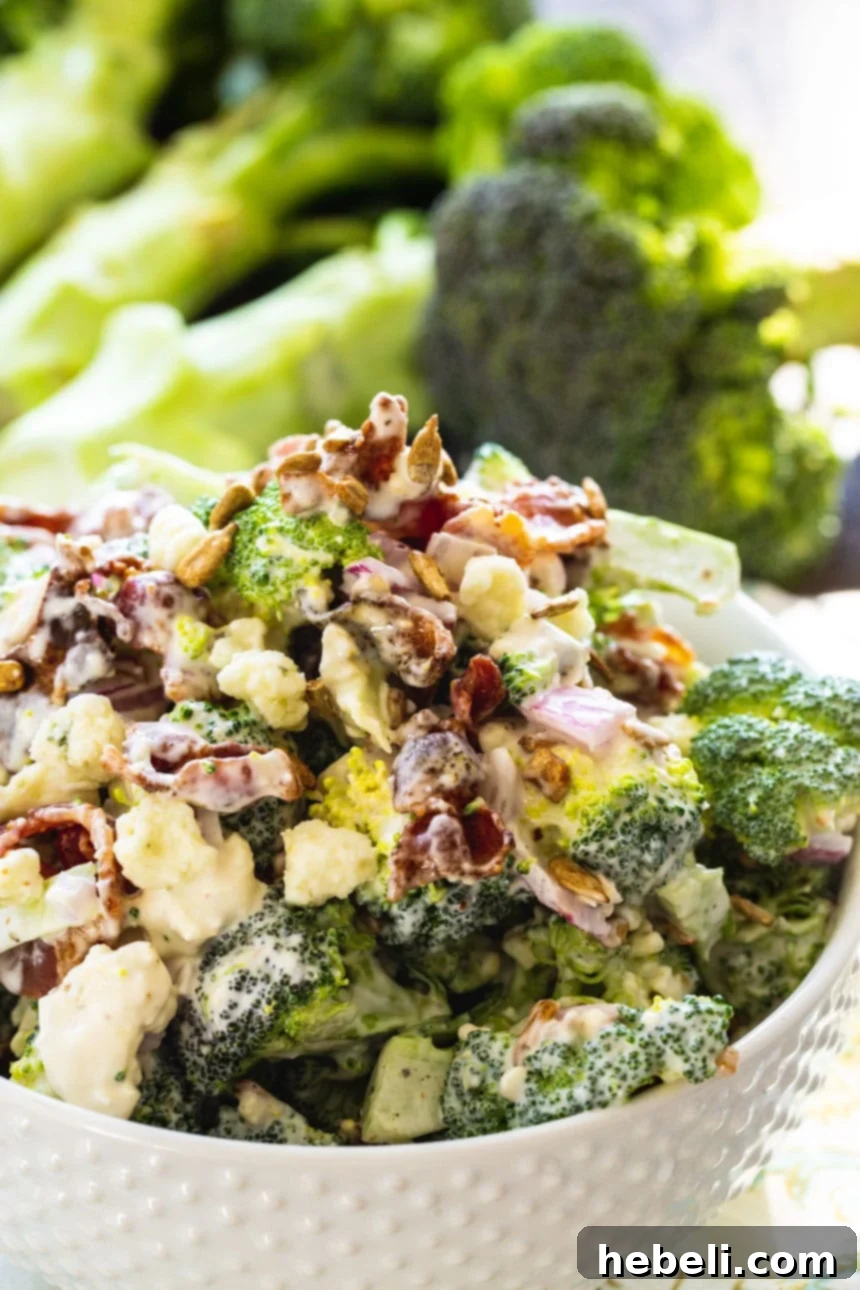 A close-up shot of Bacon Broccoli Salad with a bunch of fresh broccoli in the background, highlighting the fresh ingredients.