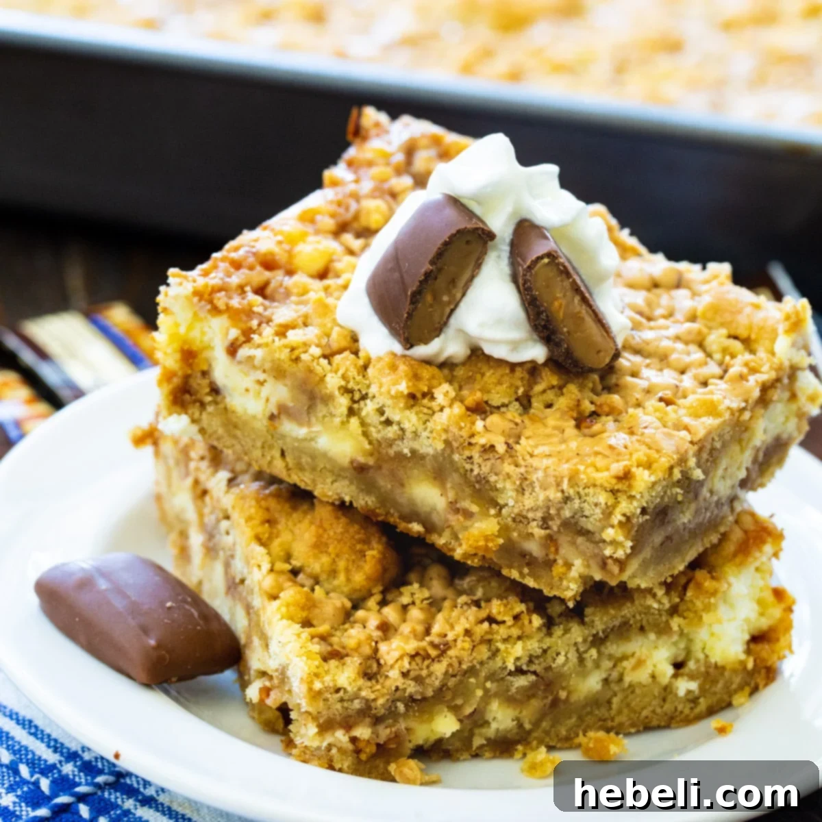 Two Toffee Cheesecake Bars stacked elegantly on a pristine white plate, showcasing their inviting golden crust and creamy interior.