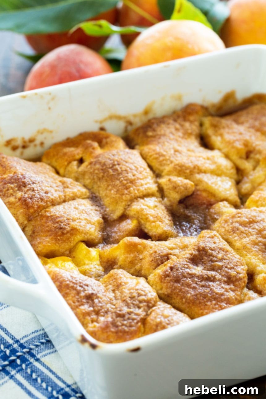 Close-up view of Peach Crescent Dumplings baking in a white ceramic dish, showcasing their golden-brown tops and bubbling syrupy sauce.