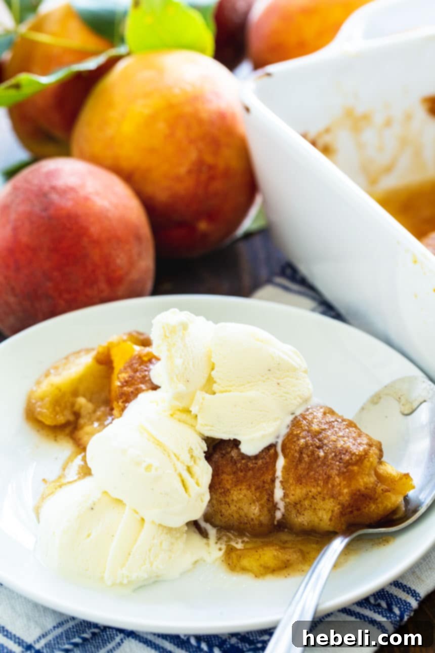 A beautifully plated Peach Dumpling, glistening with syrupy sauce, accompanied by a generous scoop of vanilla ice cream, creating a perfect dessert.