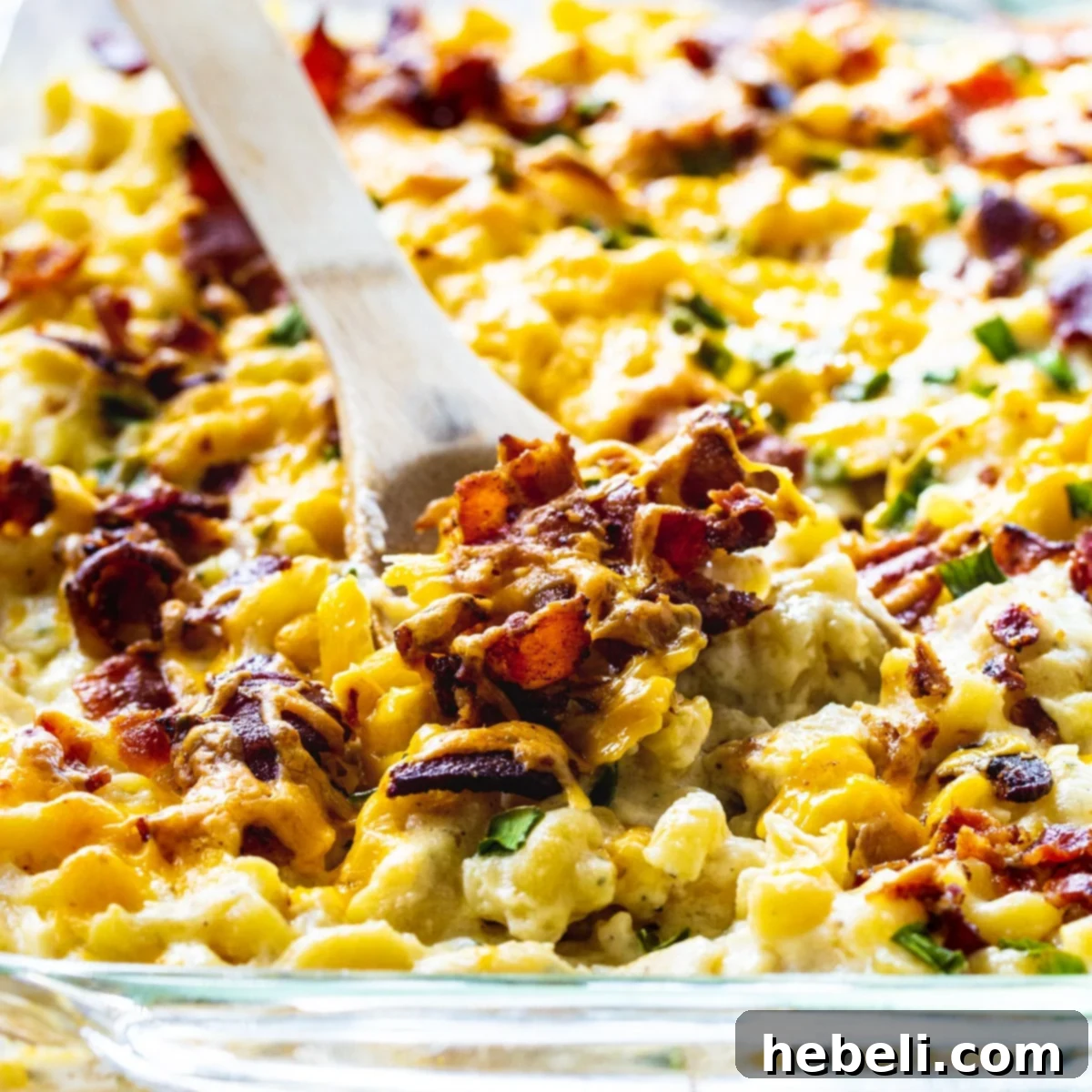Loaded Chicken Bacon and Ranch Mac and Cheese 2 Wooden spoon scooping generous portion of creamy Chicken, Bacon, and Ranch Mac and Cheese from a baking dish, showcasing melted cheese and savory ingredients.