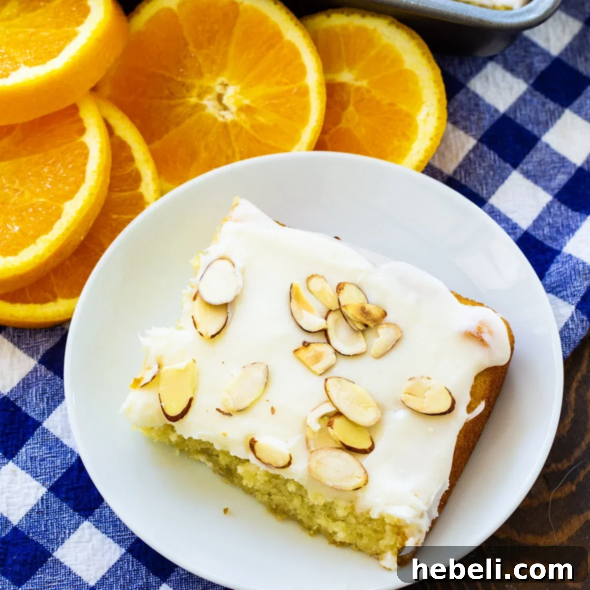 Golden Orange Almond Delight 2 A delectable slice of Orange Almond Sheet Cake on a white plate, beautifully garnished with fresh orange slices, ready to be enjoyed.
