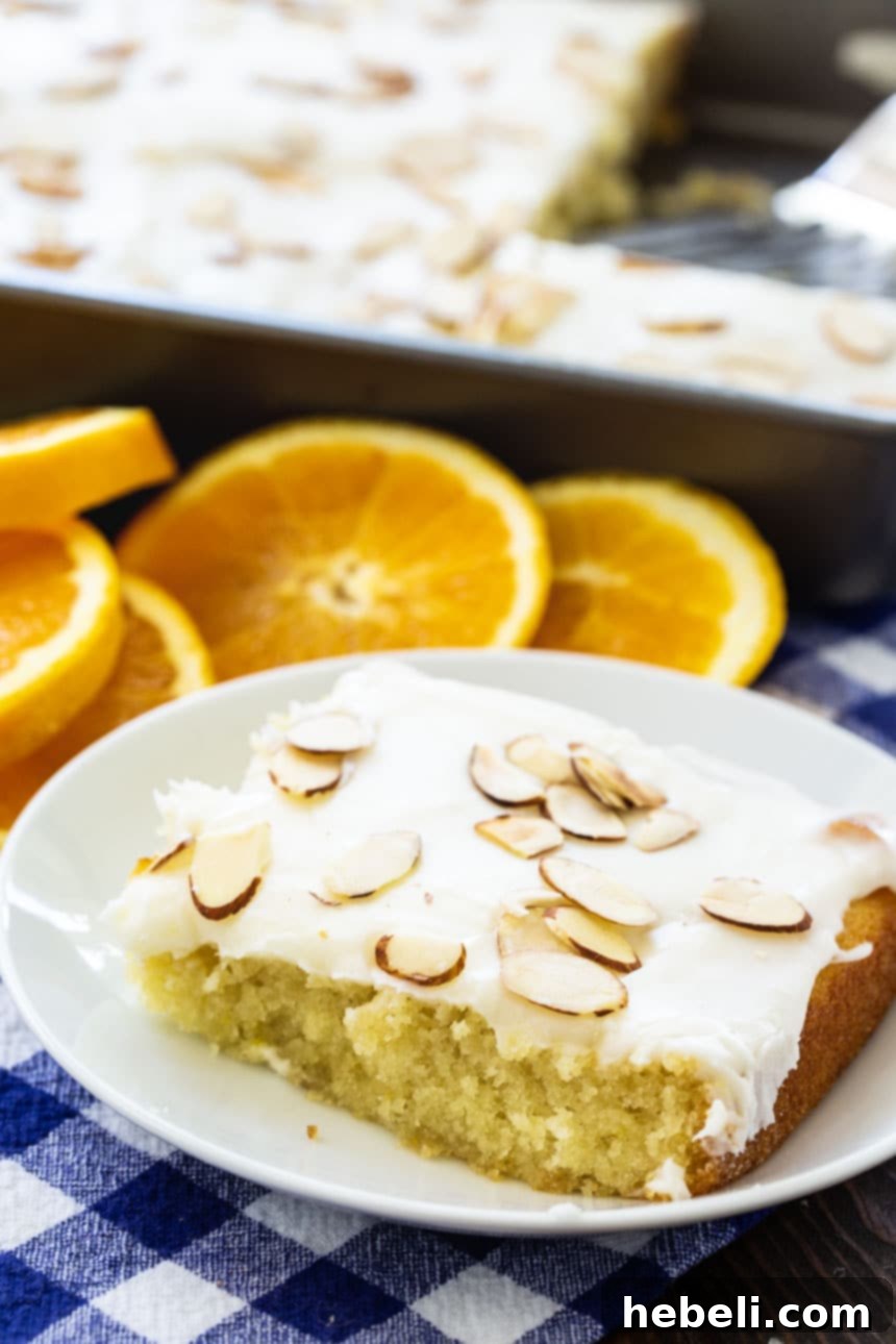 Golden Orange Almond Delight 4 A delightful slice of Orange Almond Sheet Cake resting on a white plate, with fresh orange slices beautifully arranged in the background, signaling a perfect summer dessert.