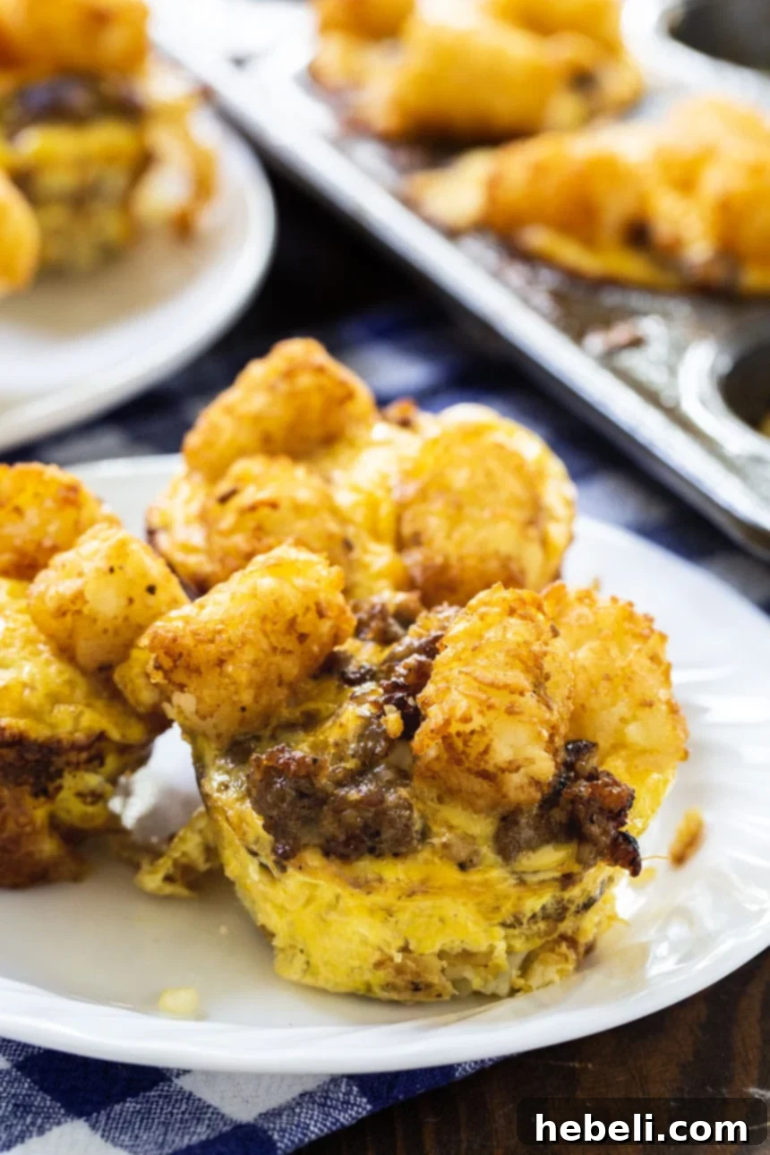 A close-up of a single Sausage and Cheese Tater Tot Cup on a white plate, highlighting its texture.