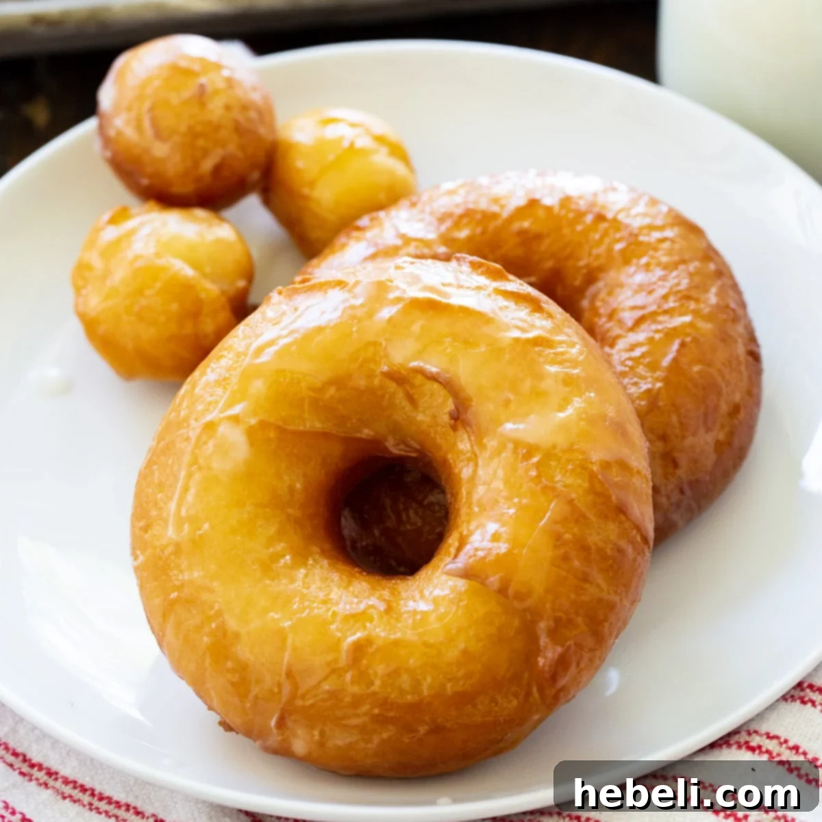 Homemade Krispy Kreme Style Doughnuts 2 Two golden-brown, glazed Copycat Krispy Kreme Doughnuts on a white plate, showcasing their fluffy texture and irresistible shine.