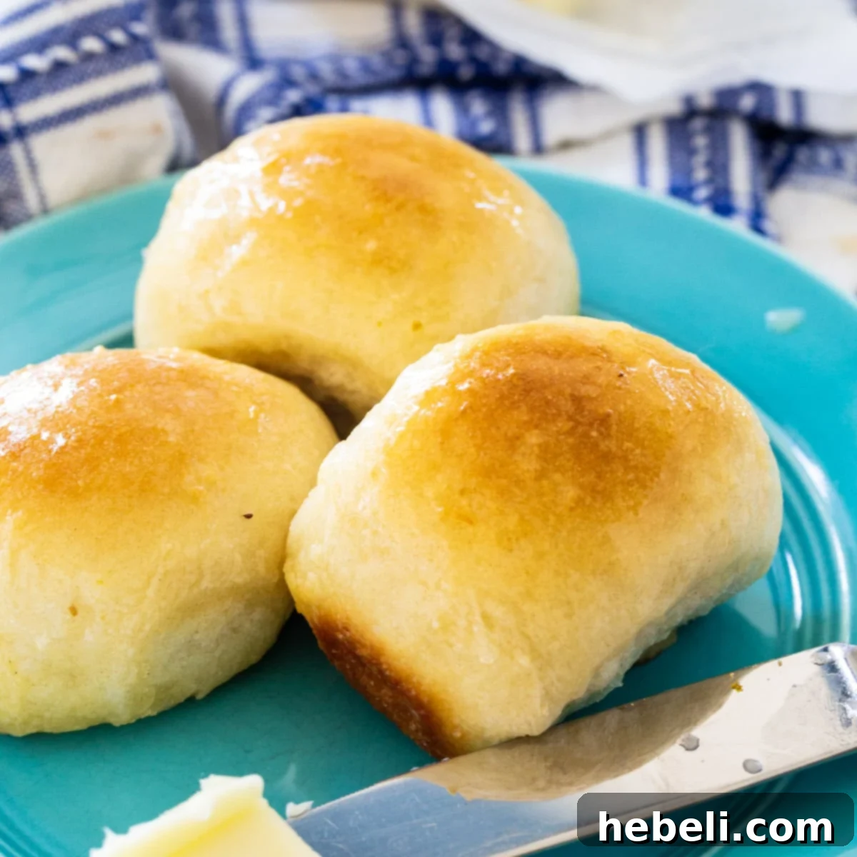 Pillowy Soft Butter Buns 2 Three golden Buttery Pan Rolls on a rustic blue plate, highlighting their soft texture.