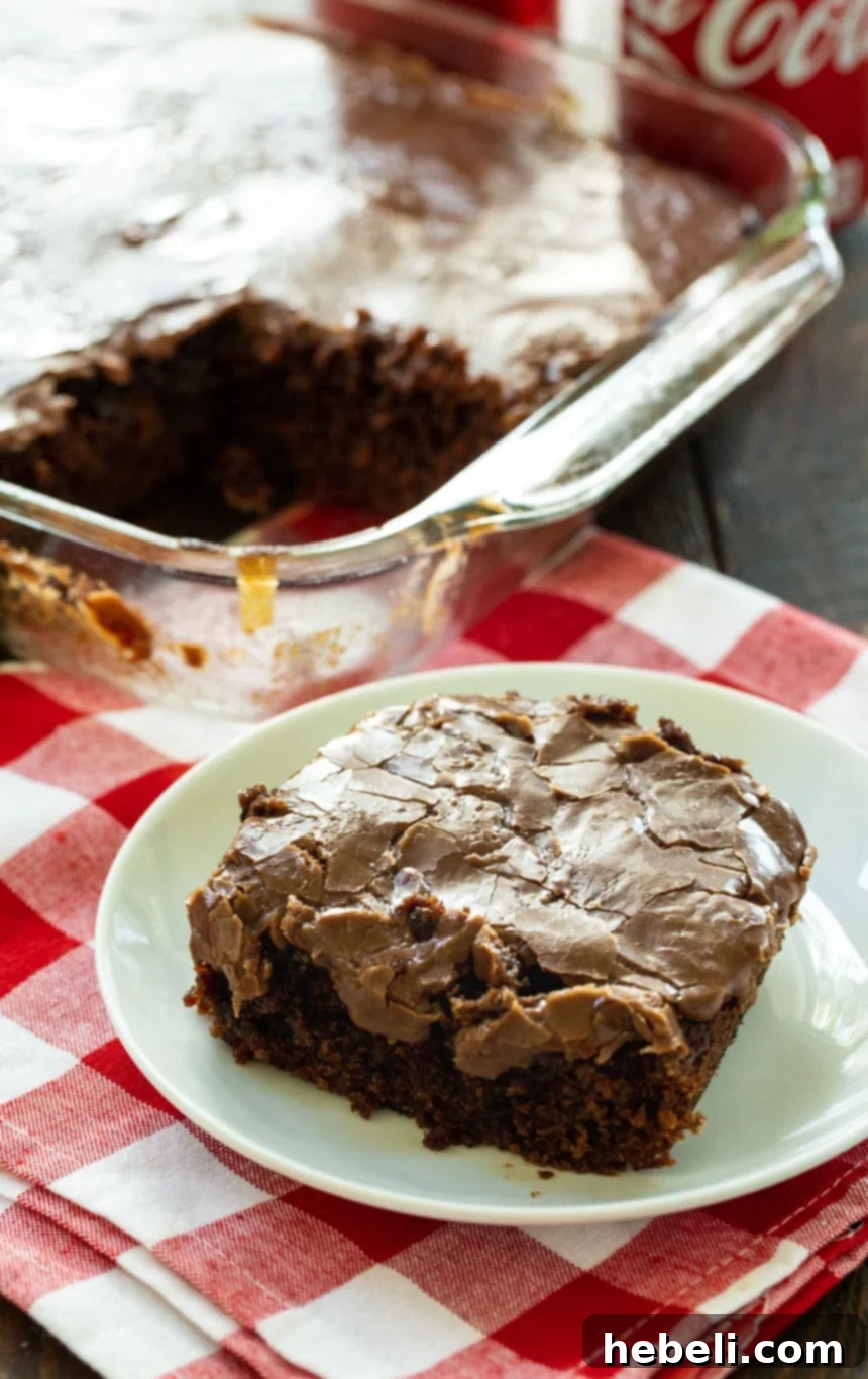 Grandma's Coca-Cola Cake 11 A slice of Classic Coca-Cola Cake on a white plate with the remaining cake in the background, beautifully frosted.