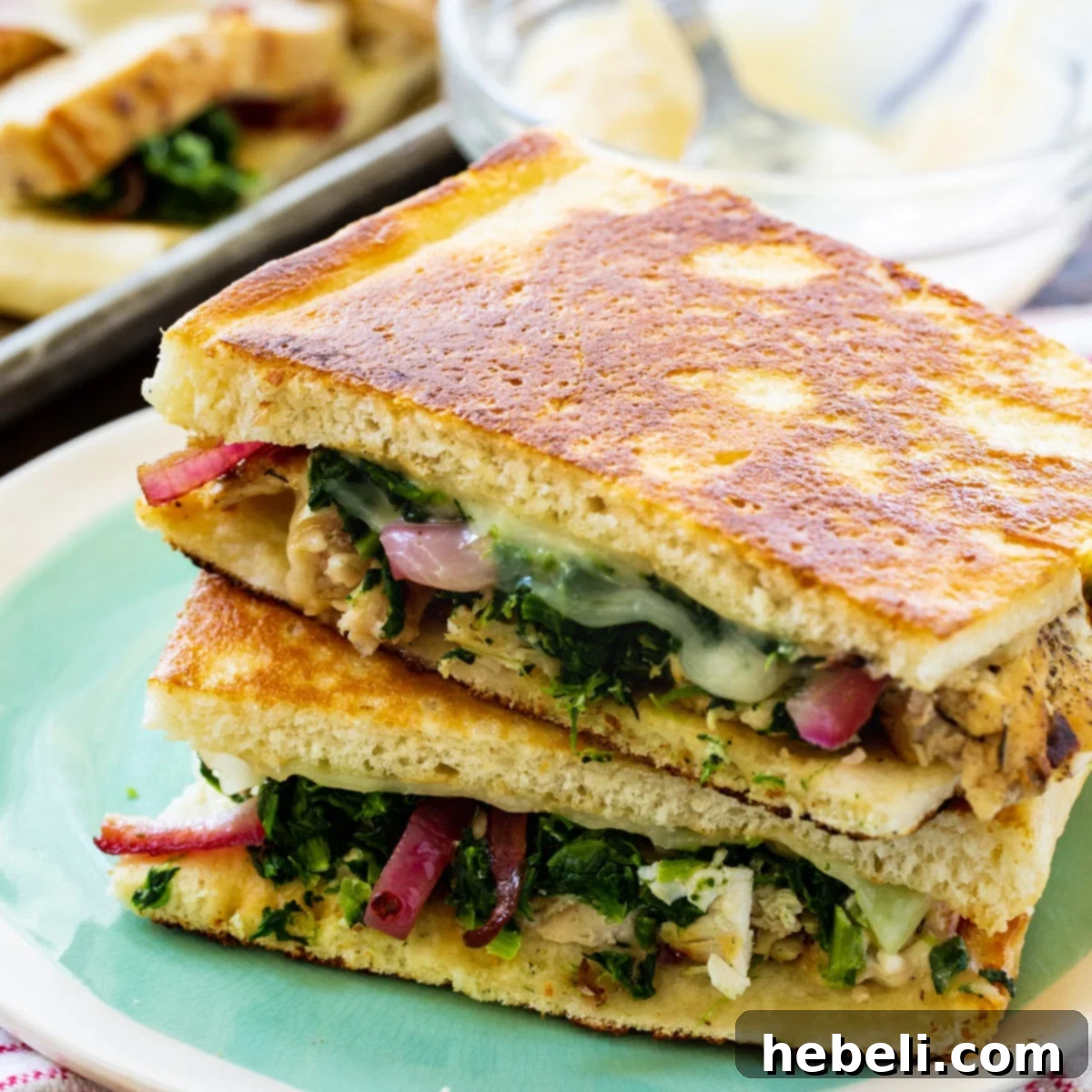 Two halves of a golden-brown Chicken Florentine Panini, stacked invitingly on a white plate, showcasing the rich filling and toasted bread.