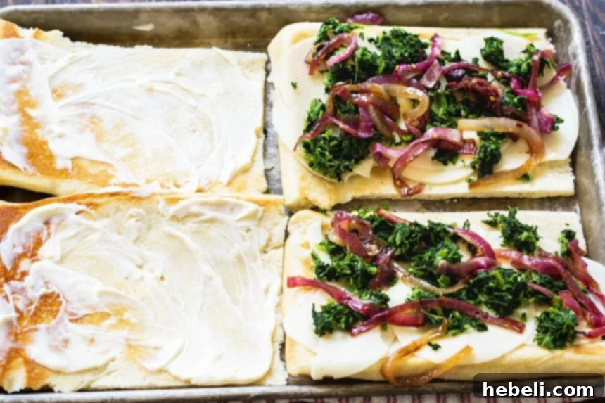 A golden-baked flatbread generously topped with a vibrant mixture of fresh spinach and sweet caramelized red onions, ready for the next layers.