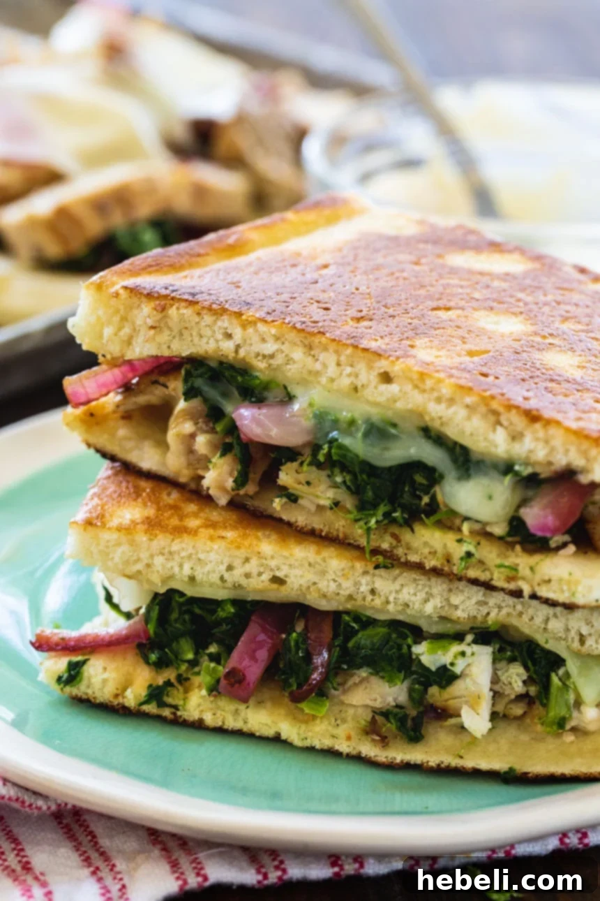 Two perfectly grilled Chicken Florentine Panini halves stacked on a white plate, showcasing crispy bread and succulent filling.