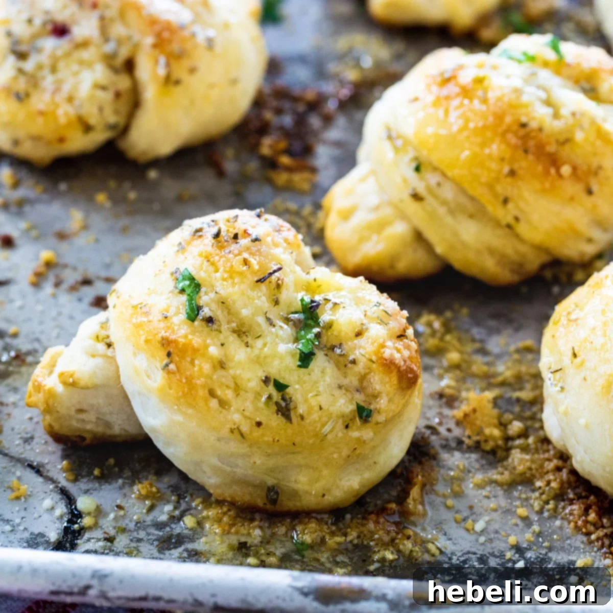 Golden brown garlic knots fresh out of the oven, arranged on a baking sheet, glistening with butter.