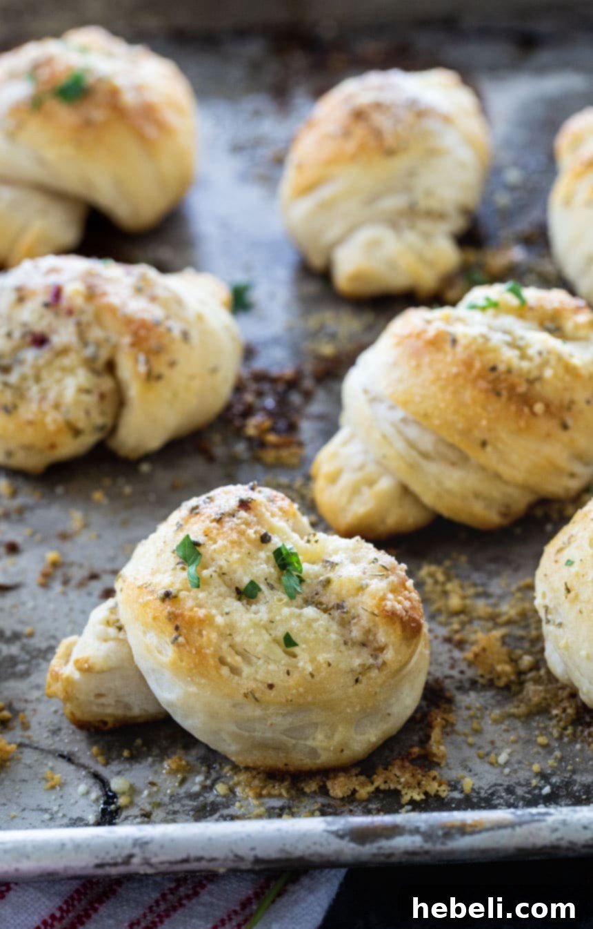 Close-up of easy garlic knots on a baking sheet, brushed with butter and herbs before baking.