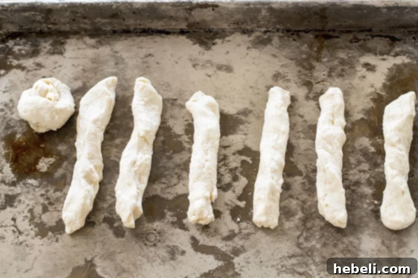 Biscuit dough pieces being rolled into thin ropes and tied into knots on a wooden surface.
