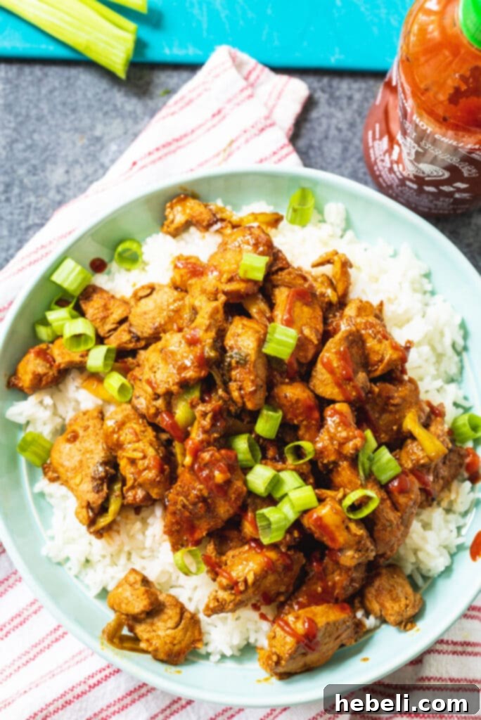 Stir-Fried Spicy Pork served over rice, with a bottle of Sriracha sauce in the background, highlighting the key ingredient.