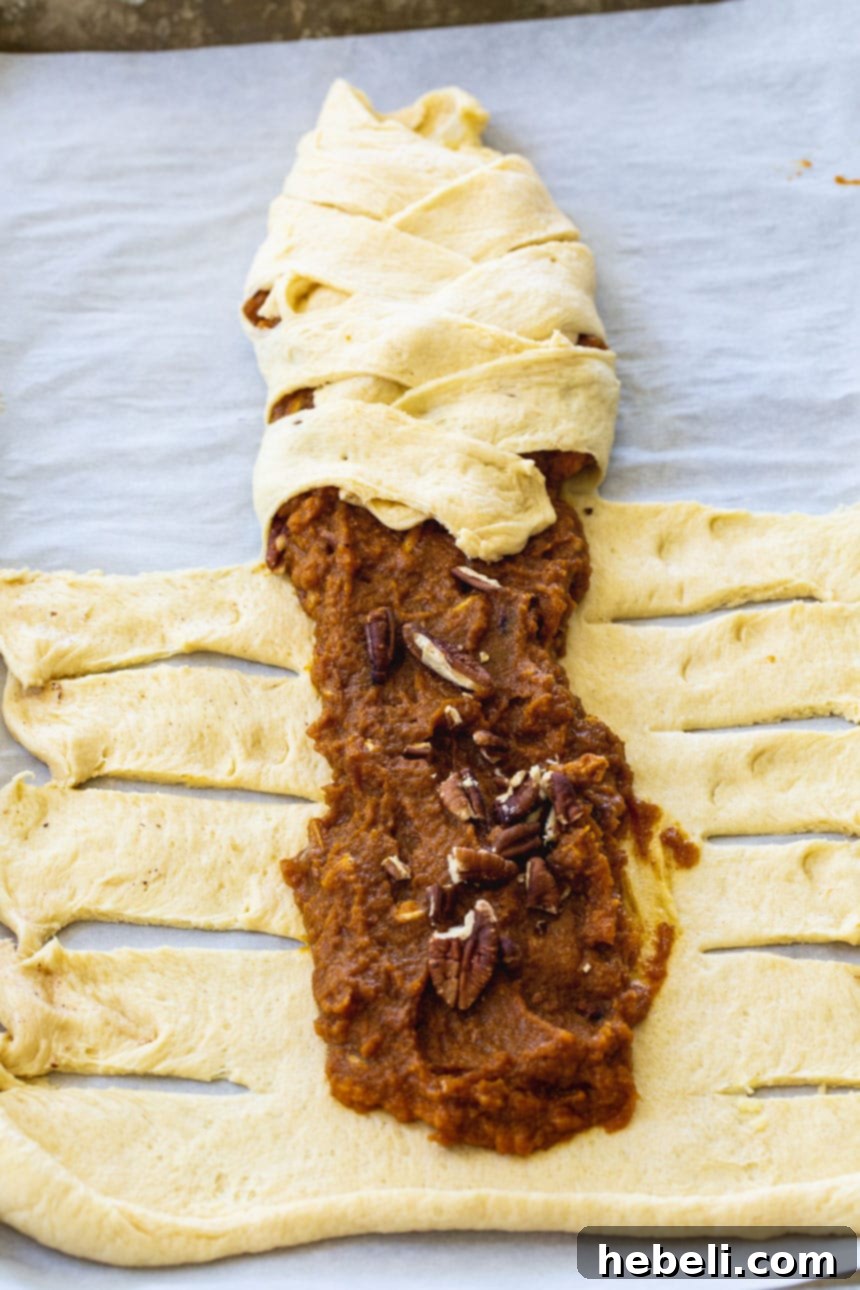 Crescent dough strips being folded over a pumpkin filling to create a braided pattern.